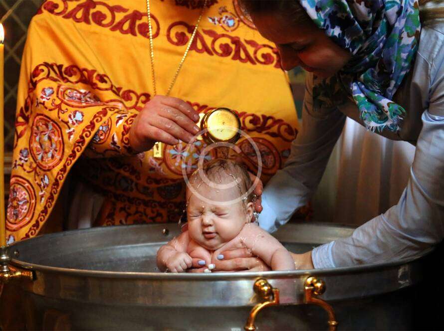 Ceremonial baby baptism in church, priest pouring water over infant in baptismal font