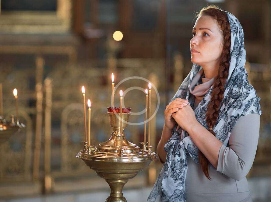 Woman in headscarf praying near lit candles in a church setting