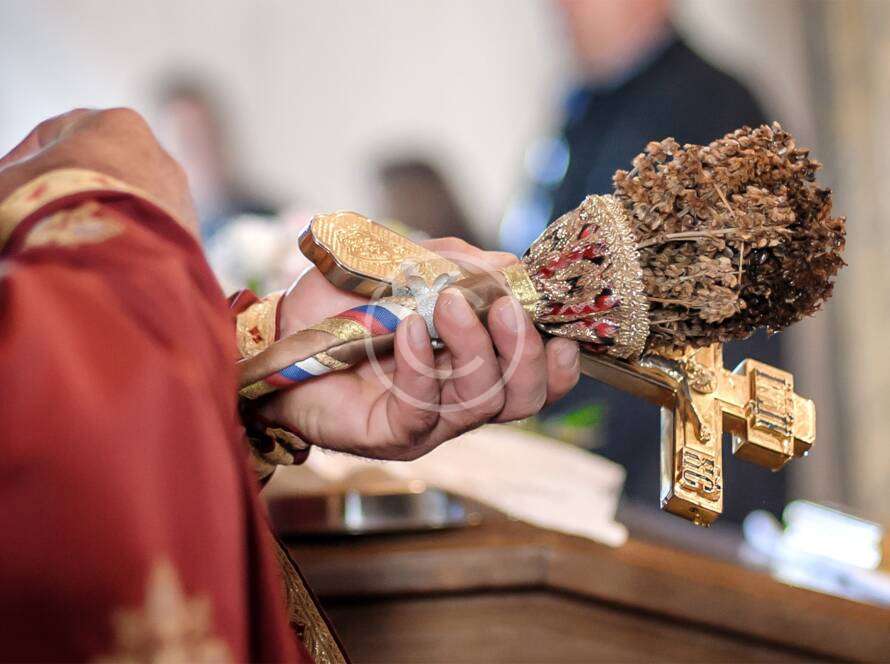 Religious ceremony with priest holding ornate gold cross and brush, close-up of sacred items in ritual context