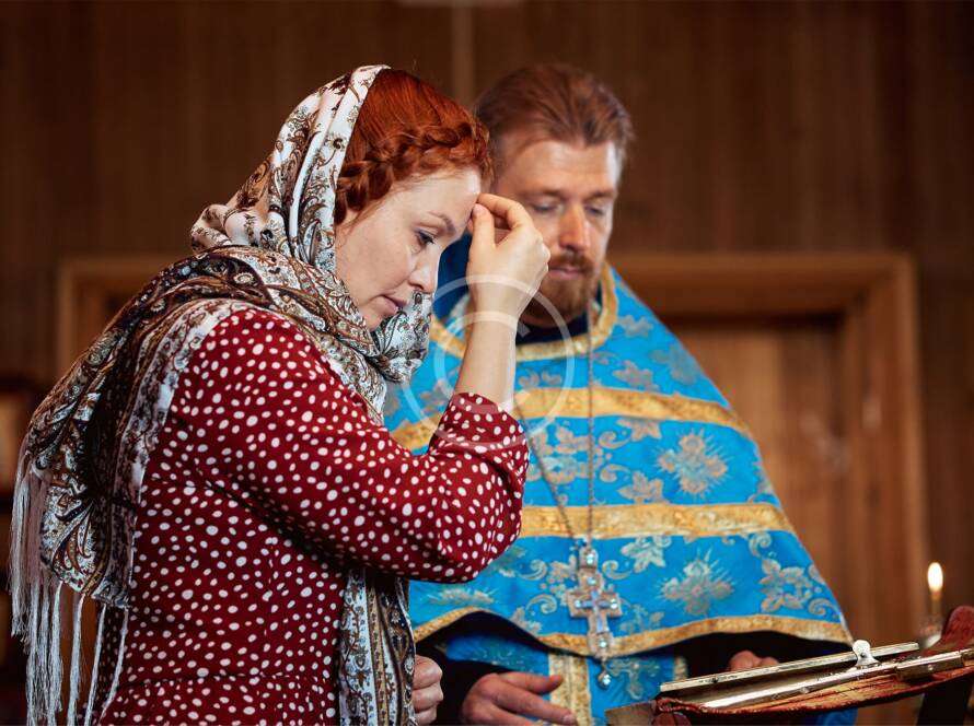 Woman praying in church with priest wearing blue and gold vestments, holding religious book, scene of faith and worship