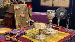 Orthodox altar with chalice, bread, ornate book, and cross on a richly decorated table in a religious setting