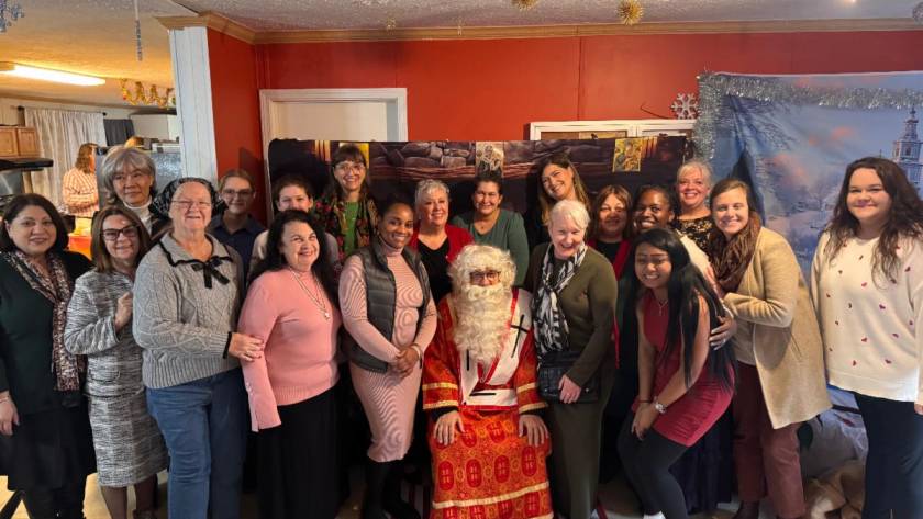 Group of smiling people posing with Santa Claus at a festive gathering indoors