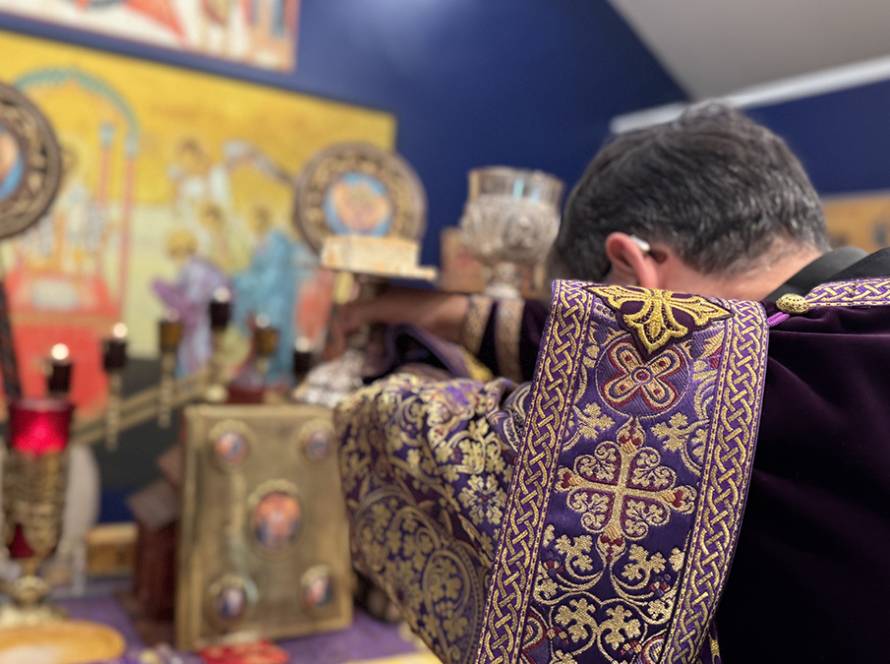 Priest in ornate purple robe conducting religious service at decorated altar