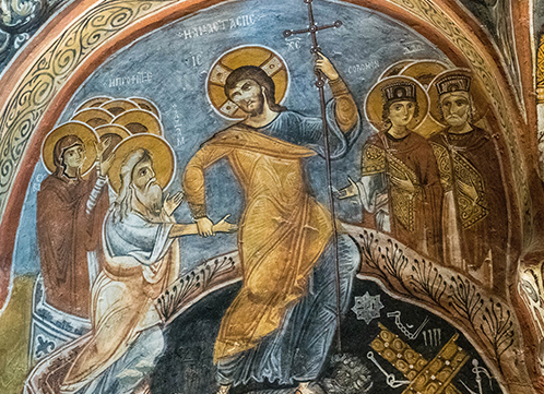 Ancient religious mural depicting a haloed figure with a cross surrounded by other haloed and crowned figures in robes