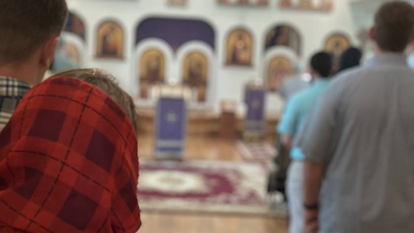 People standing in line inside a church with icons on the wall in the background