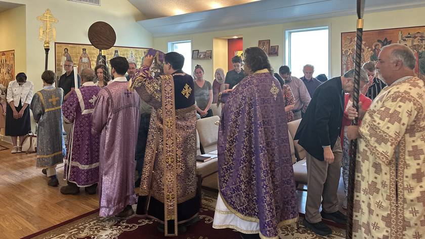 Orthodox clergy in ornate vestments lead a religious service with worshippers in a St. Mary Magdalene Church setting