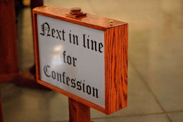Wooden church sign reading Next in line for Confession indicating order for confession queue