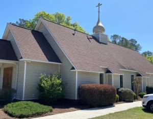 A quaint church with a golden dome and cross, surrounded by lush greenery under a clear blue sky