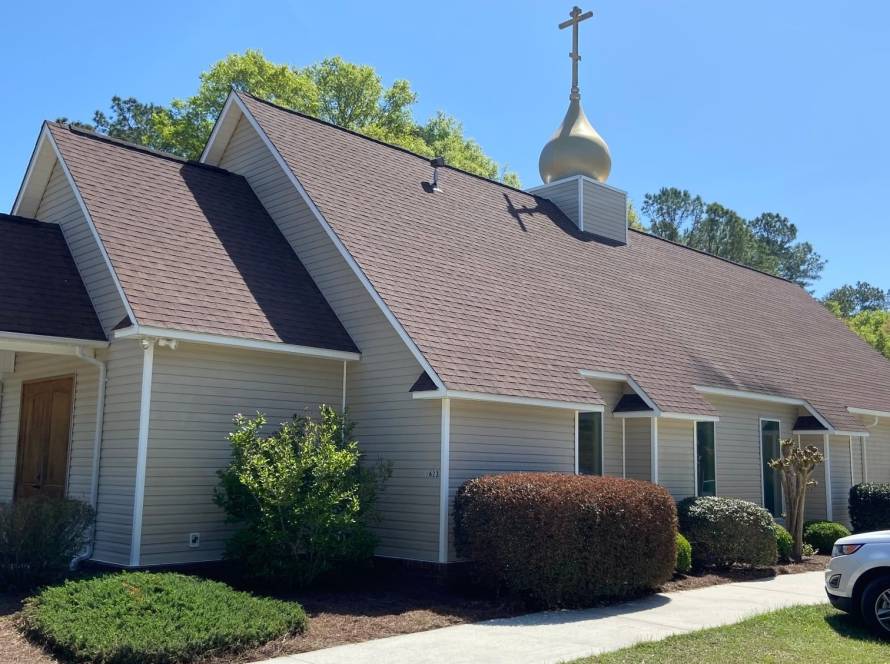 A quaint church with a golden dome and cross, surrounded by lush greenery under a clear blue sky