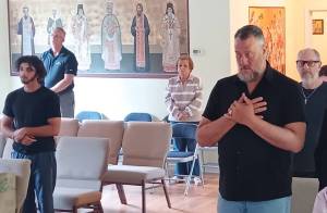 People standing in prayer during a St. Mary Magdalene church service, with religious icons on the wall