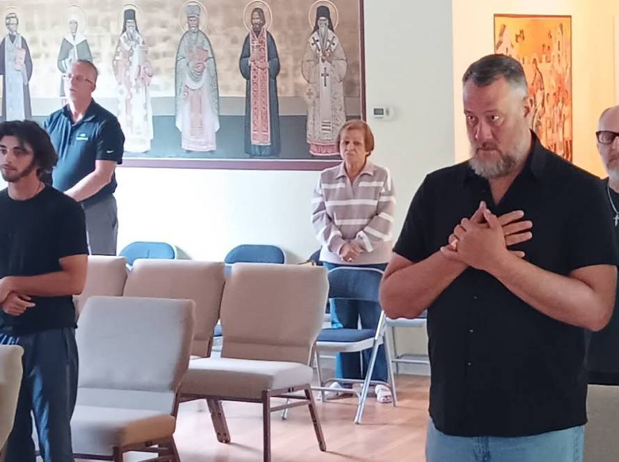 People standing in prayer during a St. Mary Magdalene church service, with religious icons on the wall