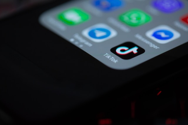 Close-up of smartphone screen displaying TikTok icon alongside other apps in dark lighting environment