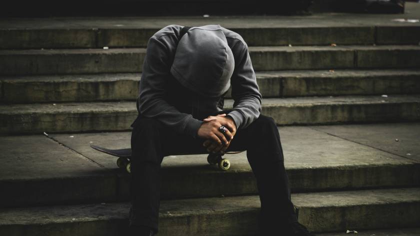 Hooded person sitting on steps with skateboard, head down, showcasing urban style and emotion