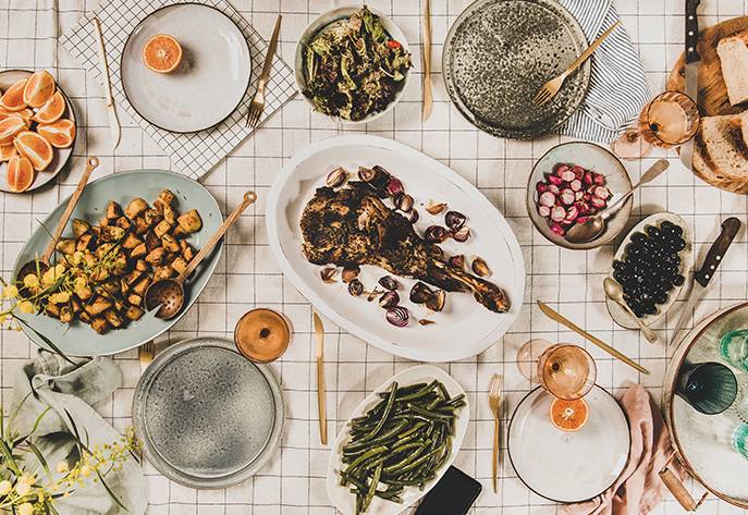 Elegant dining table with grilled lamb, roasted potatoes, fresh vegetables, and fruits arranged for a festive meal