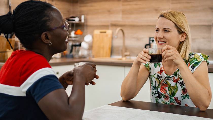 Two women enjoying coffee together in a cozy kitchen setting, smiling and engaged in conversation