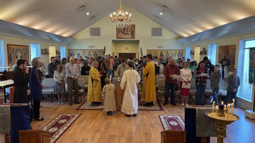 Orthodox church ceremony with congregation attending, priests in gold robes, and religious icons decorating the walls