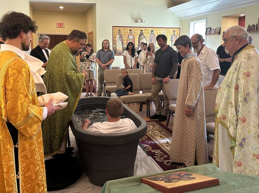 Baptism ceremony with priests and attendees in a church setting, a person is in a baptismal tub