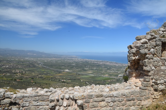 Ancient stone wall with scenic view of landscape and coastline under blue sky with clouds
