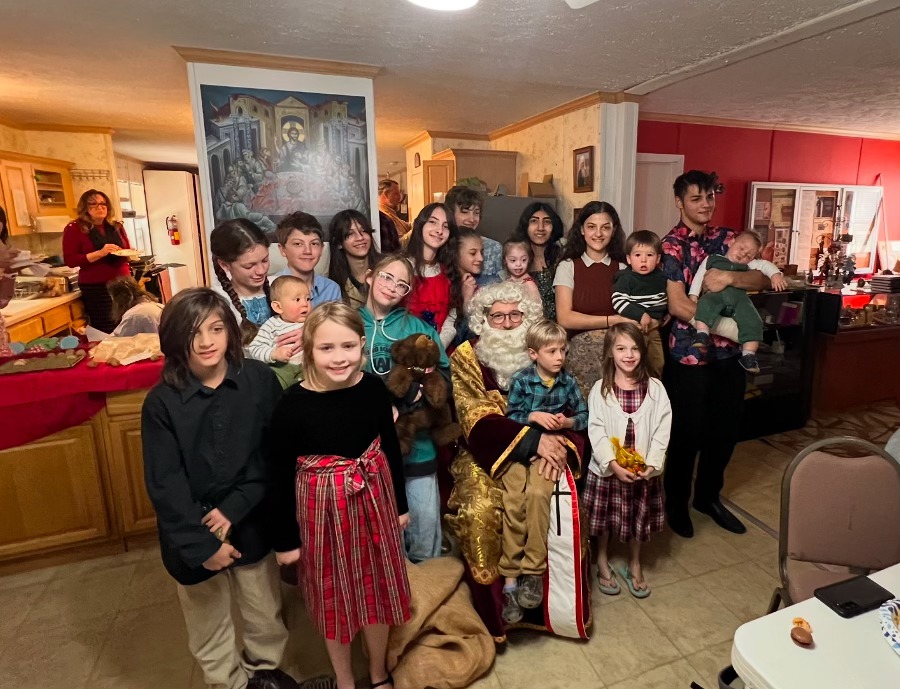 Group of children and adults celebrating with a Santa Claus figure in a cozy indoor setting