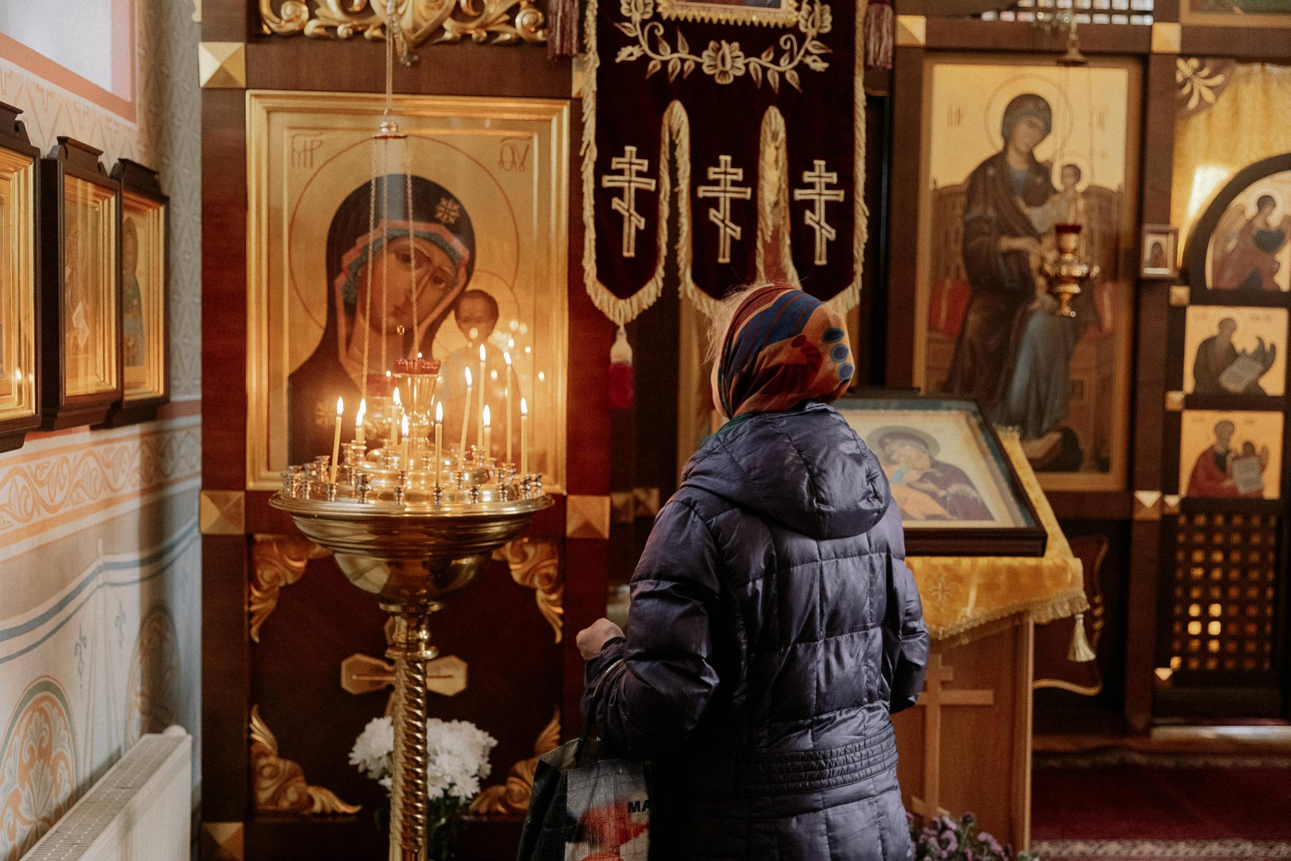 Woman lighting candles in a church with religious icons in the background