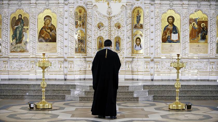 Priest standing before ornate icons in a beautiful church setting during a religious ceremony