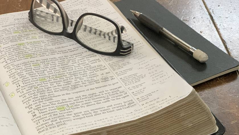 Open Bible with pen and glasses on a table, highlighting text and study notes for in-depth reading session