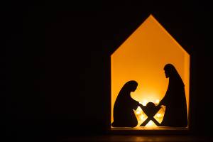Nativity scene silhouette with Mary, Joseph, and baby Jesus in manger illuminated by warm light
