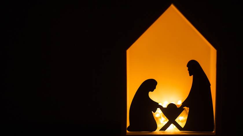 Nativity scene silhouette with Mary, Joseph, and baby Jesus in manger illuminated by warm light