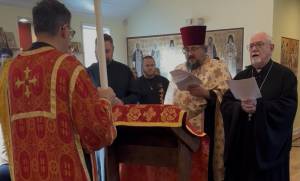 Priests in red and black robes perform a religious service with hymn sheets in a decorated church setting