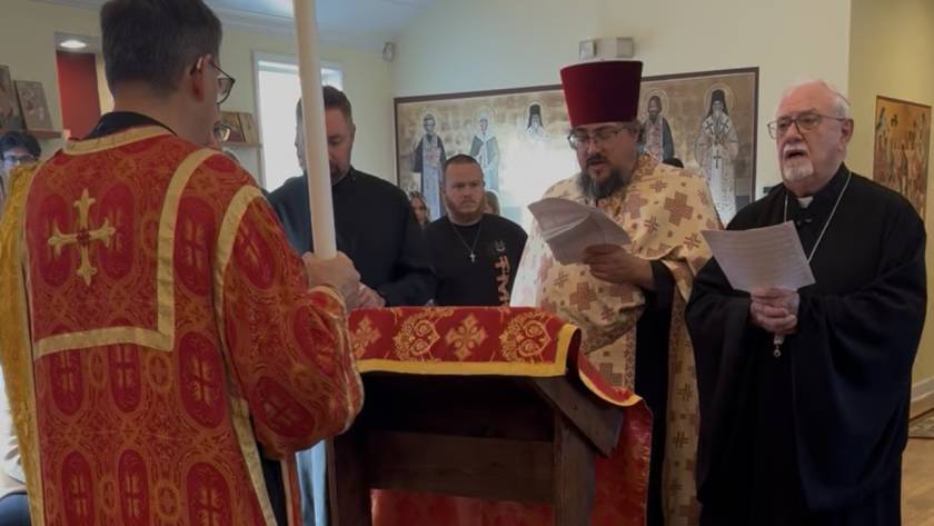 Priests in red and black robes perform a religious service with hymn sheets in a decorated church setting