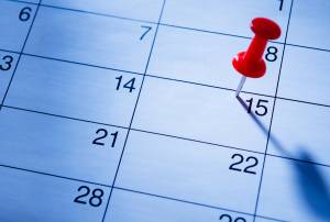 Red pushpin marking date on calendar sheet highlighting the 15th, scheduled event or reminder concept