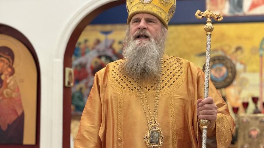 Orthodox priest in ornate gold vestments holding a staff during a religious ceremony in a decorated church setting