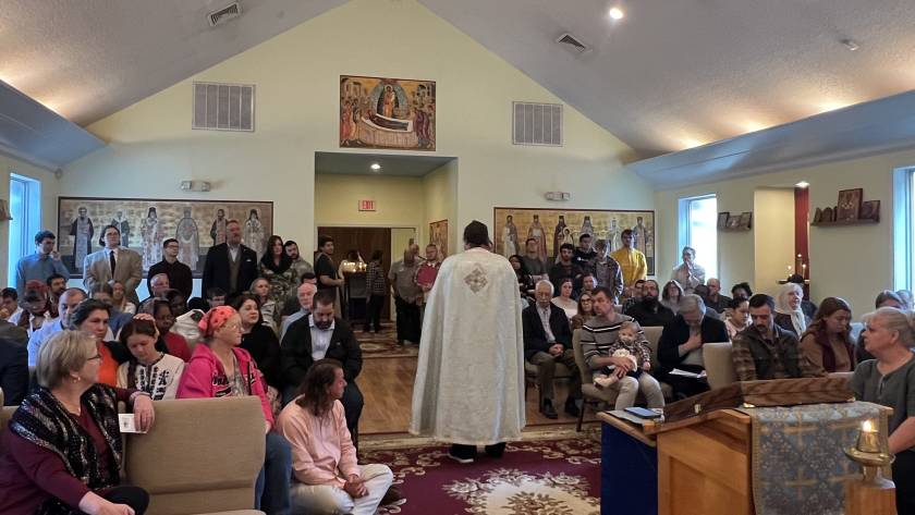 A priest conducting a service in a packed church with attentive congregation members seated and standing
