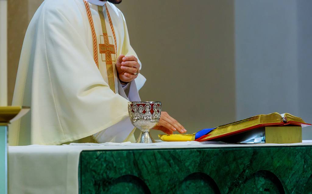 Priest preparing communion with chalice and open Bible on altar during religious ceremony in church