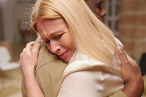 Woman with blonde hair emotionally hugging someone, showing support and comfort in a heartfelt moment