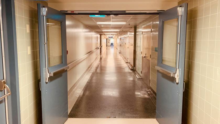 Open double doors leading to a long hospital corridor with emergency exit sign overhead