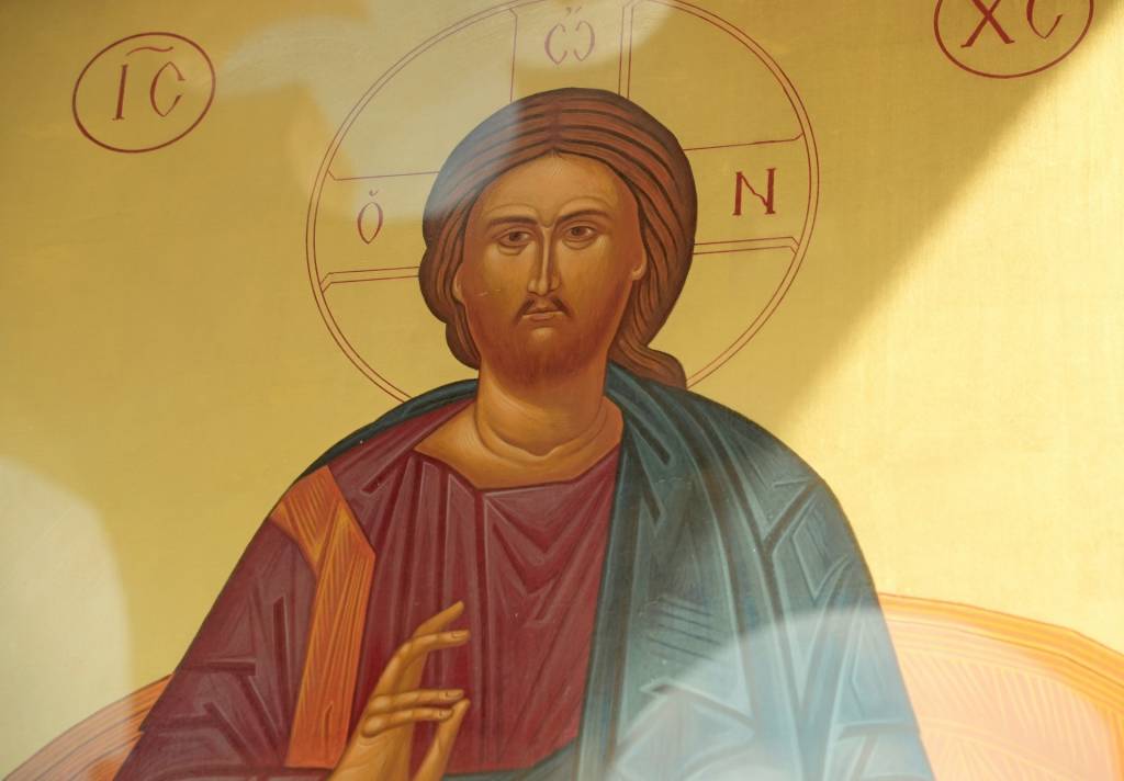 Icon of religious figure with halo and hand raised in blessing gesture, traditional art style with vivid colors