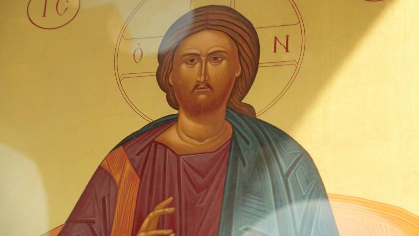 Icon of religious figure with halo and hand raised in blessing gesture, traditional art style with vivid colors