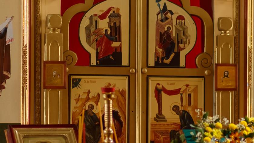 Ornate religious icons with vivid colors and gold accents inside a church setting with flowers and framed pictures