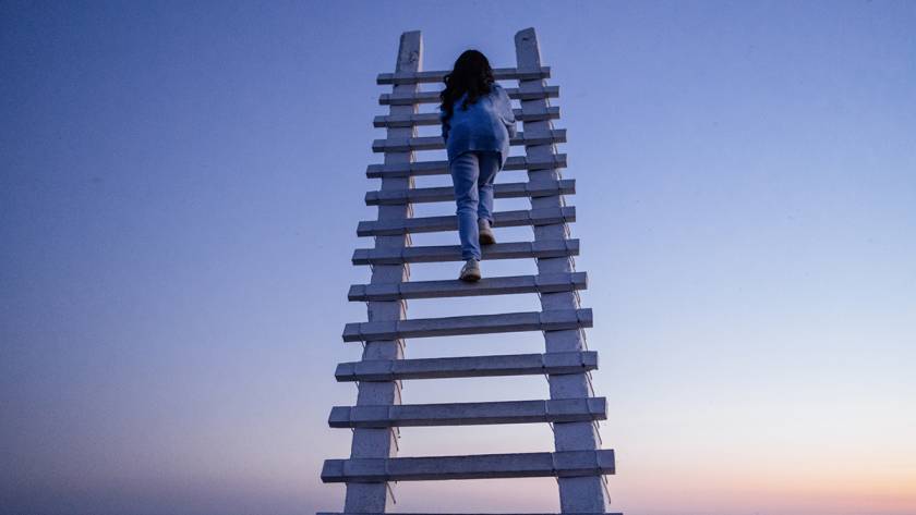 Person climbing large white ladder at sunrise with a clear sky background