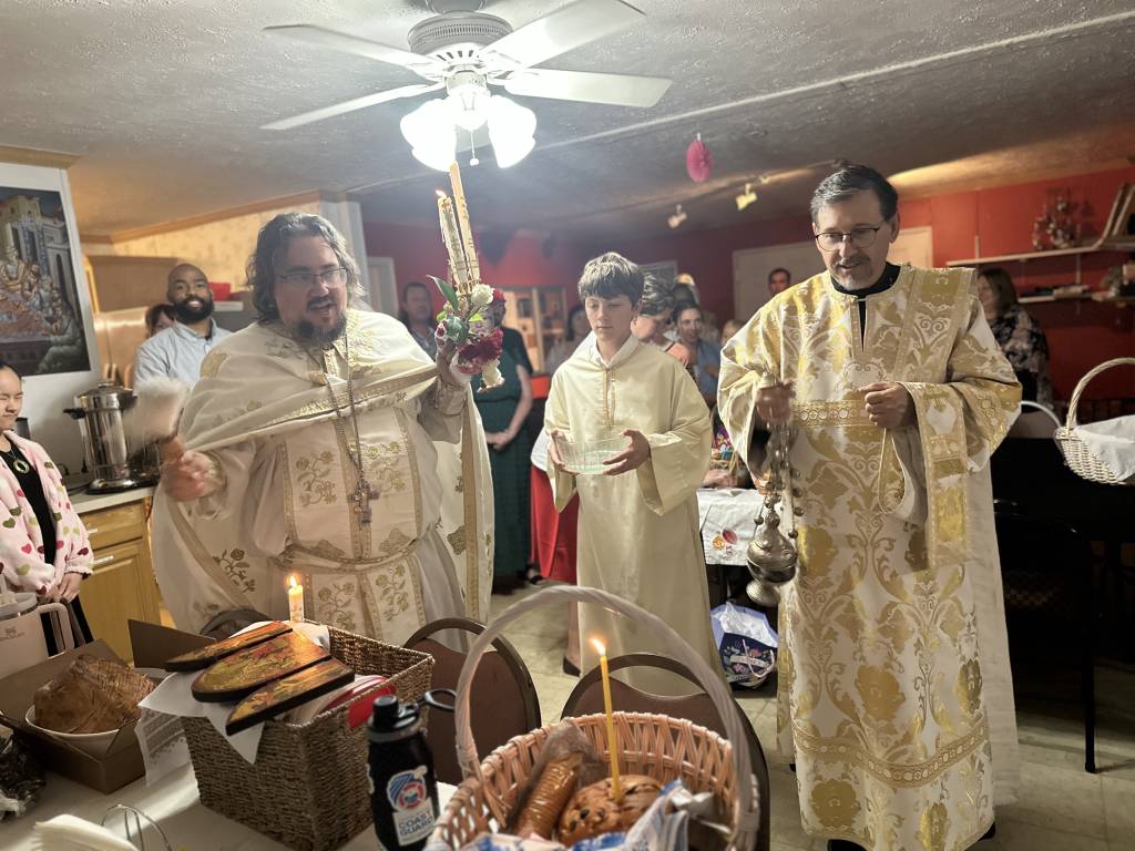 Priests in ornate robes perform blessing ceremony in warmly decorated room with candles and traditional items