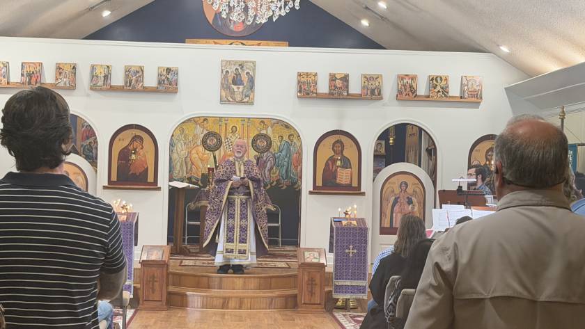 Orthodox church service with priest in purple vestments, congregation and religious icons, under a chandelier