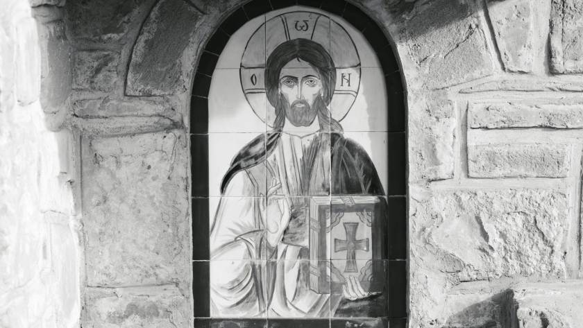 Black and white mural of Jesus Christ on stone wall, featuring halo and cross, Byzantine art style