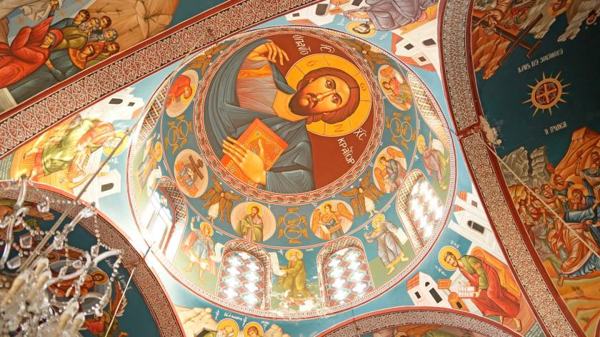 Colorful religious frescoes on a domed church ceiling depicting Christ and various biblical scenes in vibrant detail