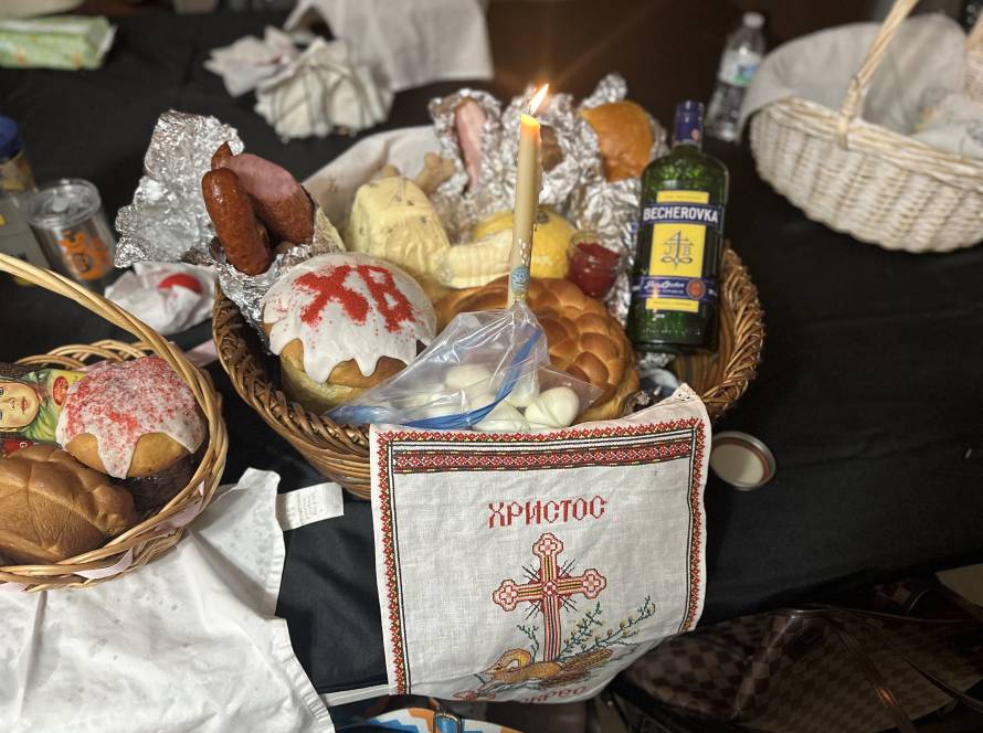 Easter basket with candle, decorated cakes, meats, bread, and Becherovka bottle on table with embroidered cloth