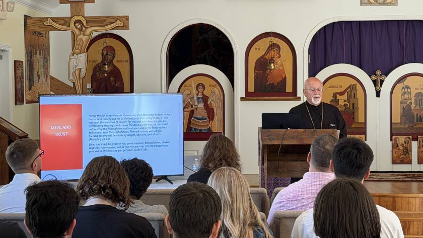 Speaker presenting at church with audience, screen showing Love and Trust, religious icons displayed on walls