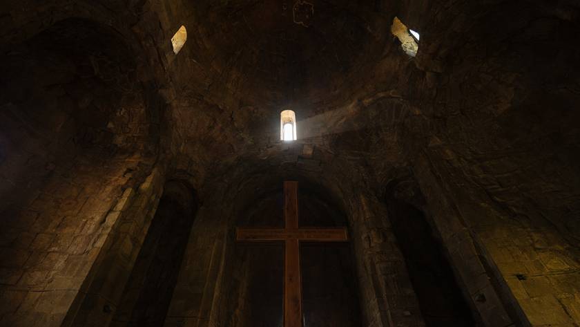 Dramatic church interior with light streaming through windows and casting shadows over a large wooden cross