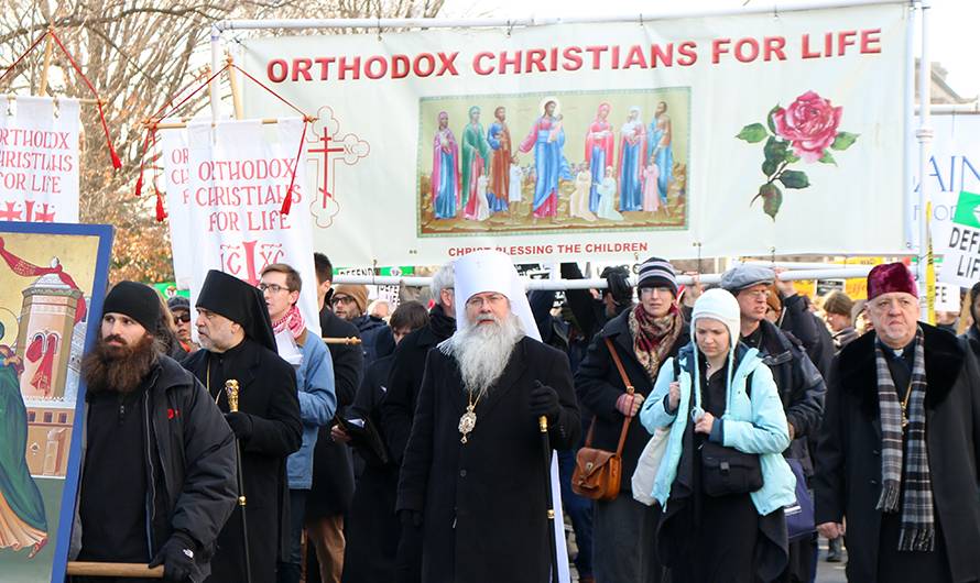Orthodox Christians hold signs and banners at a pro-life march with a religious icon at the forefront