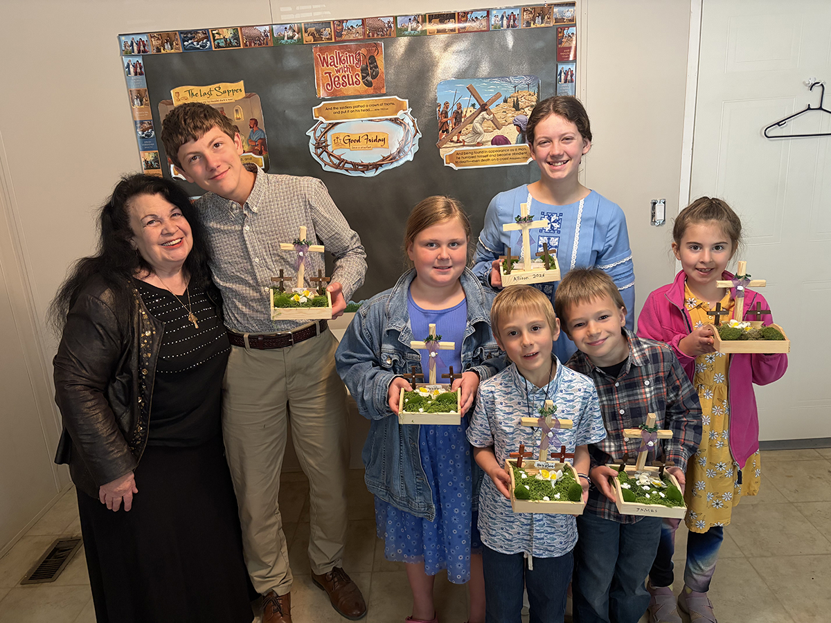 Group of children and a woman smiling and holding crafted crosses at an educational event indoors