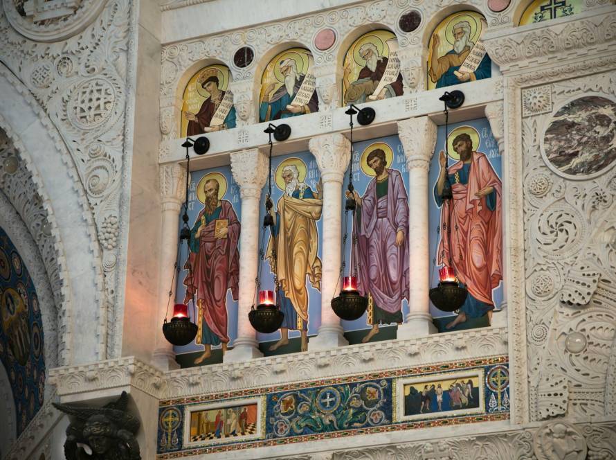 Intricate religious frescoes and ornate carvings in a historic church interior display vibrant saint depictions
